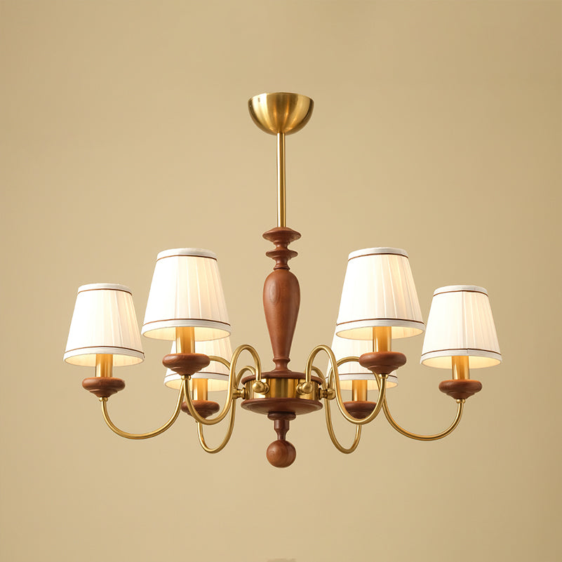 Six-light Clérachic chandelier in gold and walnut, hung from a short brass canopy with the shades lit against a sand-coloured backdrop.