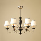 Chrome and black Clérachic chandelier with six lit shades and a black turned stem, on a plain sand-coloured background.