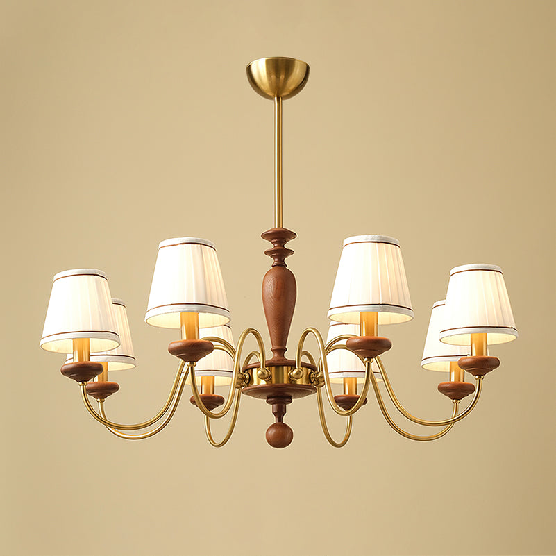 Eight-light gold and walnut Clérachic chandelier, its two tiers of brass arms and pleated shades lit on a beige backdrop.