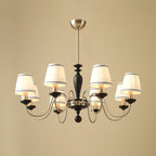 Eight-light chrome and black Clérachic chandelier with white pleated shades, a black stem and chrome arms, on a beige backdrop.