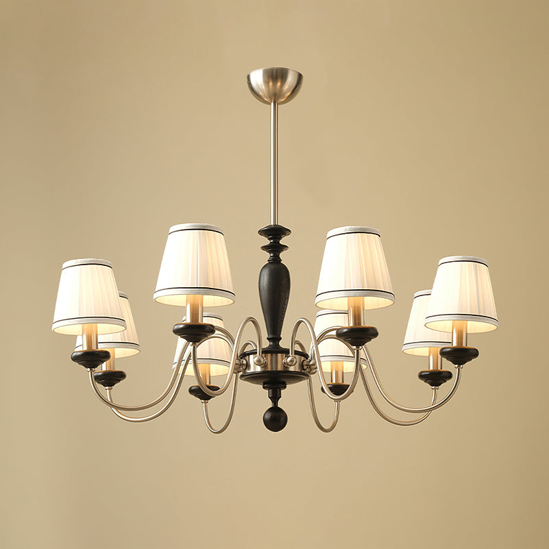 Eight-light chrome and black Clérachic chandelier with white pleated shades, a black stem and chrome arms, on a beige backdrop.