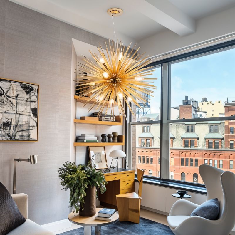 Clérachic gold spike chandelier lit in front of a tall city window, above a wooden desk and shelves.