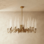 Clérachic round brass chandelier with slender clear bubbled glass shades on wavy arms, hung from a rod against a limewash wall.