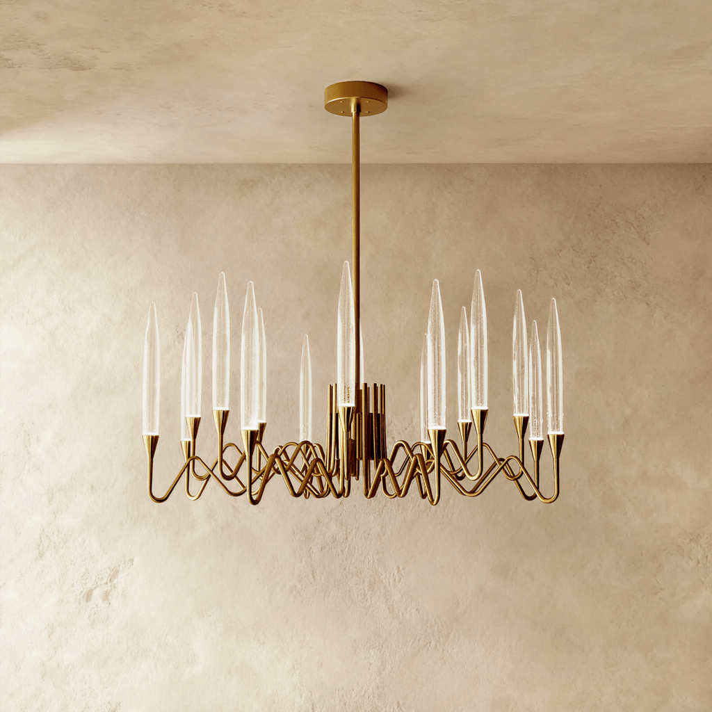 Clérachic smaller round brass chandelier with tapered clear glass candles on looping arms, centred in a warm plaster-wall room.