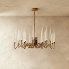Clérachic smaller round brass chandelier with tapered clear glass candles on looping arms, centred in a warm plaster-wall room.