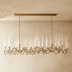 Clérachic long linear brass chandelier on two rods and a rectangular canopy, with many glass spikes over wavy arms, limewash wall behind.