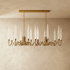 Clérachic compact linear brass chandelier with twelve clear glass shades on looping arms, hung from two rods on a rectangular canopy.