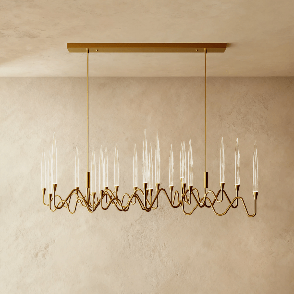 Clérachic linear brass chandelier with clear glass candle shades on rippling arms, hung from a rectangular canopy above a plaster wall.