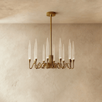 Clérachic small round brass chandelier with twelve clear glass candle shades on looping arms, hung from a rod and round canopy.
