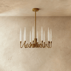 Clérachic round brass chandelier with twelve tapered glass shades on wavy arms, a gold finish against a warm limewash wall.