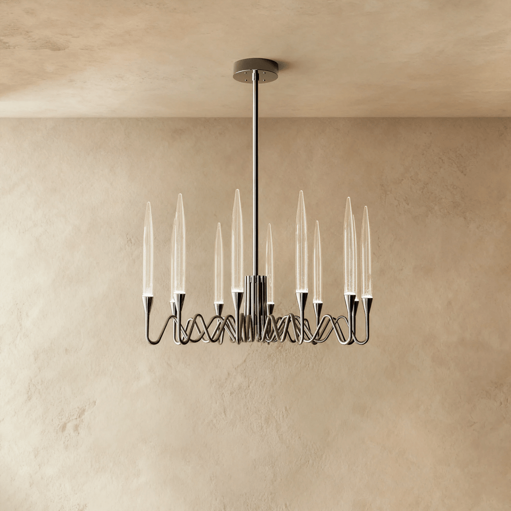 Clérachic round chandelier in a polished silver finish with twelve clear glass shades on looping arms, against a limewash wall.