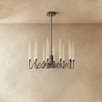 Clérachic round chandelier in a polished silver finish with twelve clear glass shades on looping arms, against a limewash wall.