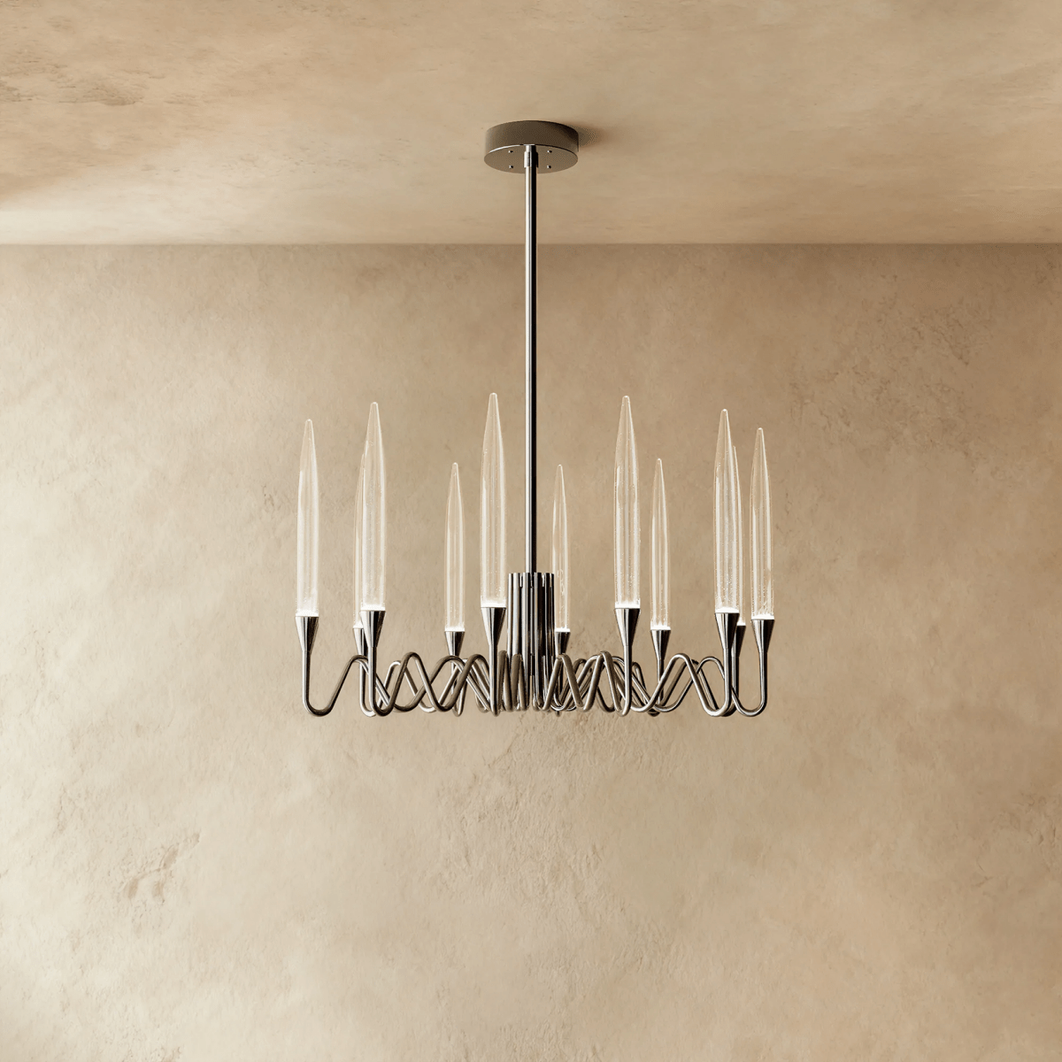 Clérachic round chandelier in a polished silver finish with twelve clear glass shades on looping arms, against a limewash wall.