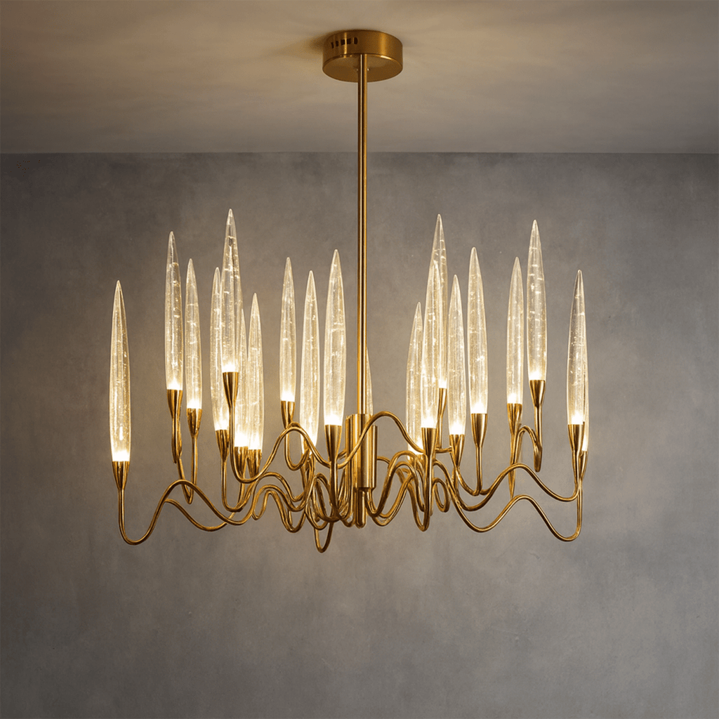 Clérachic round brass chandelier lit warm, its bubbled glass shades glowing above wavy arms, against a grey wall.