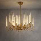 Clérachic round brass chandelier lit warm, its bubbled glass shades glowing above wavy arms, against a grey wall.