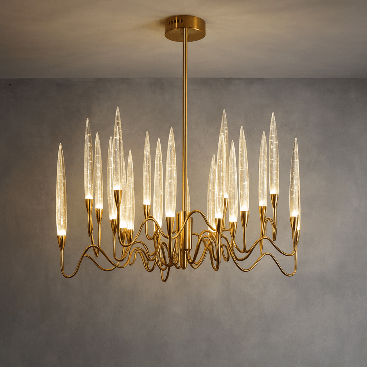 Clérachic round brass chandelier lit warm, its bubbled glass shades glowing above wavy arms, against a grey wall.