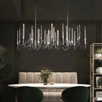 Clérachic long linear chandelier in a silver chrome finish with slim glass spikes, hung over a dining table in a dark room.