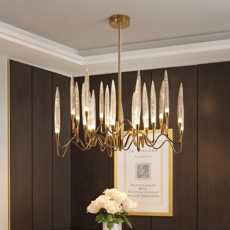 Clérachic round brass chandelier with lit glass shades in a dark panelled room, with white roses and a framed print beneath.