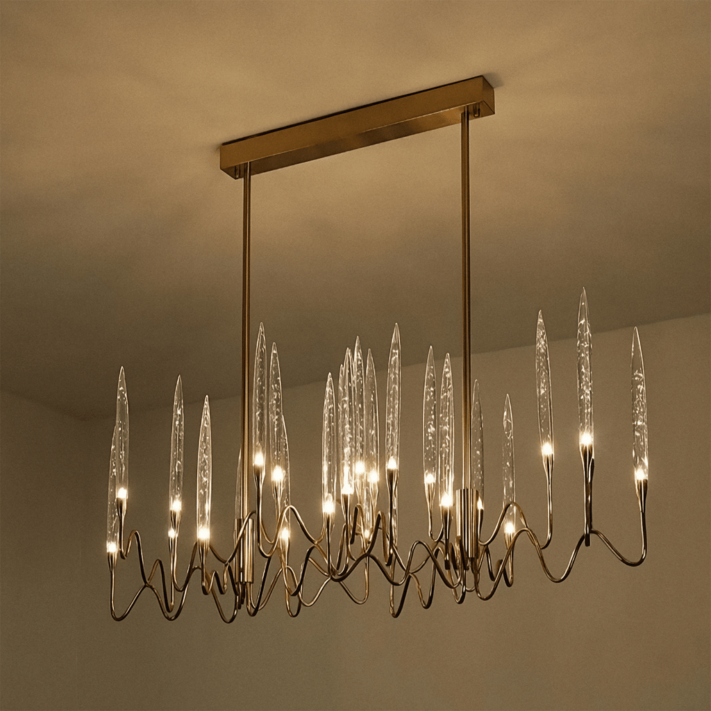 Clérachic linear brass chandelier lit warm on a rectangular canopy, its clear glass shades glowing against a softly lit ceiling.