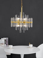Clear glass rods and brass bars of this Clérachic chandelier set against a dark grey wall, above a round white table and cups.