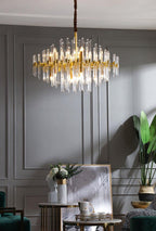 Above a dark grey panelled wall, this Clérachic chandelier hangs lit, with a plant and a framed picture on a side table below.