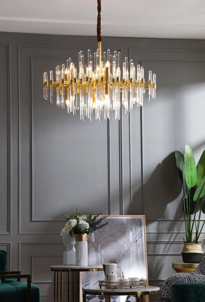 Above a dark grey panelled wall, this Clérachic chandelier hangs lit, with a plant and a framed picture on a side table below.