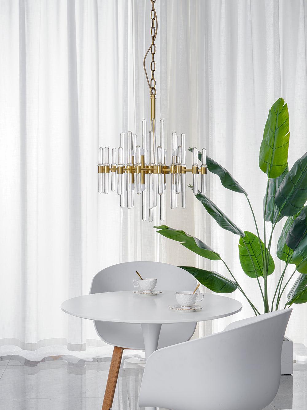 Slimmer Clérachic chandelier on a chain with a few tall glass rods, hanging above a white round table beside a leafy plant and sheer curtains.