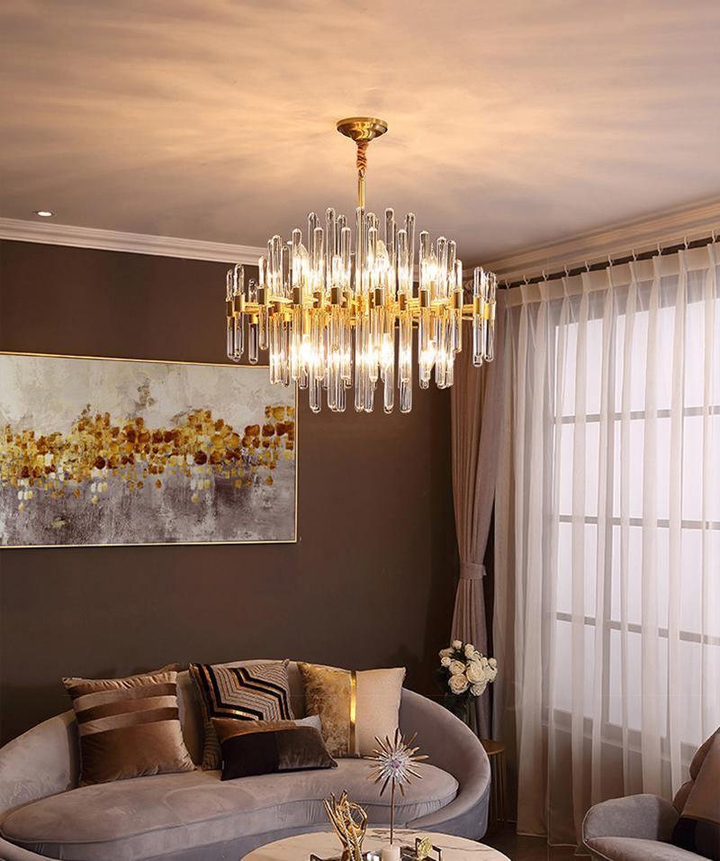 A Clérachic brass chandelier with clear glass rods glowing under a cream ceiling, above a sofa with patterned cushions and a golden painting.