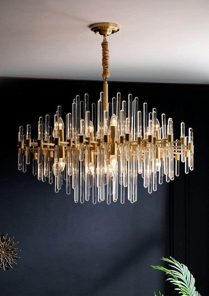 Seen from the side against a deep blue-black wall, this Clérachic chandelier shows its glass rods in tiers, with a plant at the corner.
