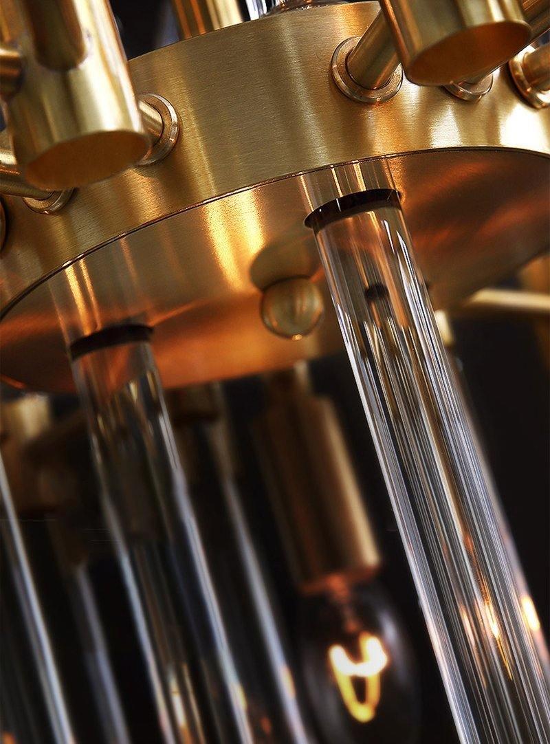 Close view of the brushed brass ring, tube sockets and long glass rods on this Clérachic chandelier, with a lit bulb glowing below.