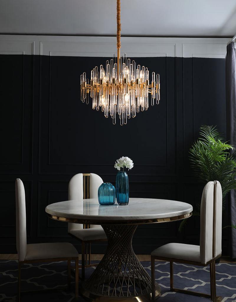 This Clérachic chandelier hangs above a round marble-top dining table with cream chairs, against a dark panelled wall and a tall plant.