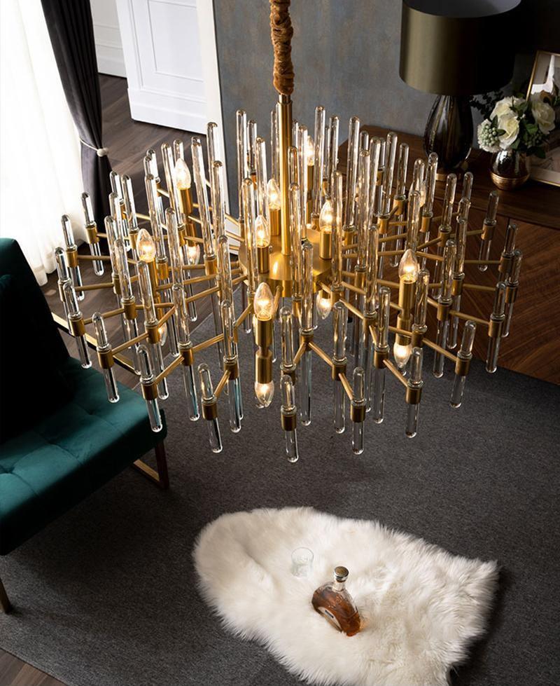 Looking up into a very large Clérachic brass chandelier, its many arms and candle-style bulbs spread above a green armchair and sheepskin rug.