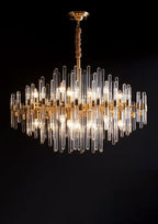 A Clérachic chandelier of brass bars and clear glass rods lit on a black background, its tiers forming a diamond-shaped outline.