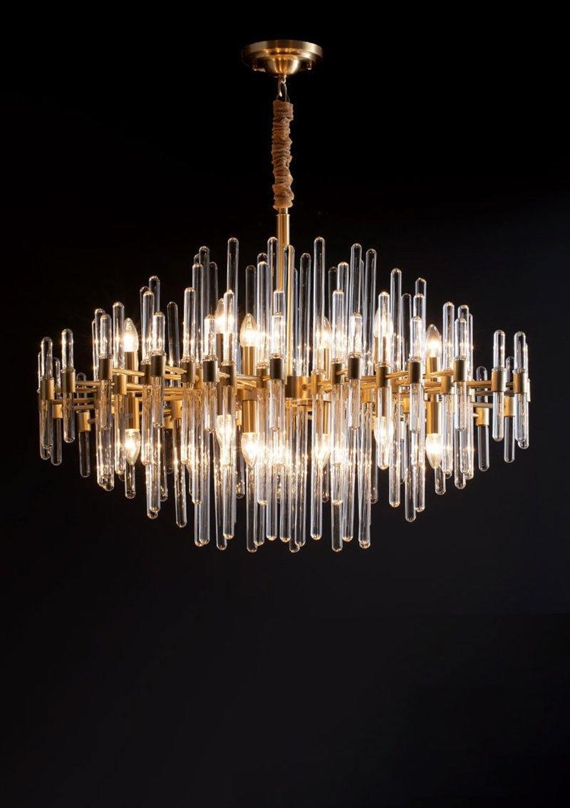 A Clérachic chandelier of brass bars and clear glass rods lit on a black background, its tiers forming a diamond-shaped outline.
