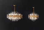 Two sizes of this Clérachic chandelier side by side on a black backdrop, both with clear glass rods and brushed brass frames.