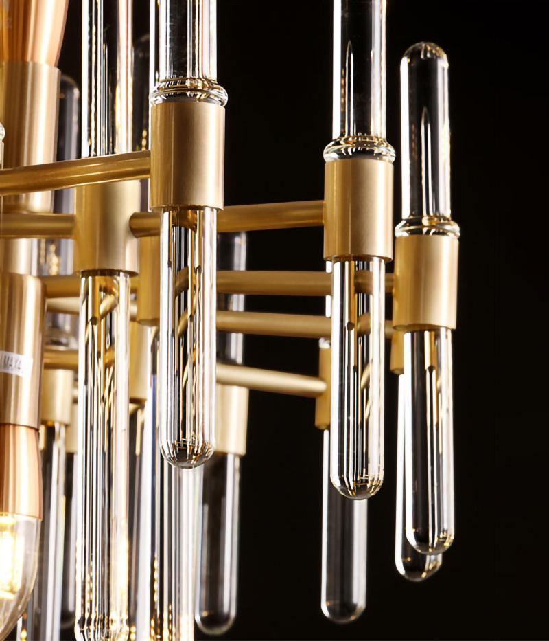 Close view of brass sockets, horizontal bars and clear glass tubes on this Clérachic chandelier, with a bulb inside one tube.