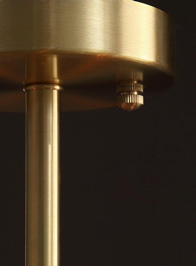 Close view of the brushed brass ceiling plate and rod of this Clérachic chandelier, with a small brass screw below the plate.