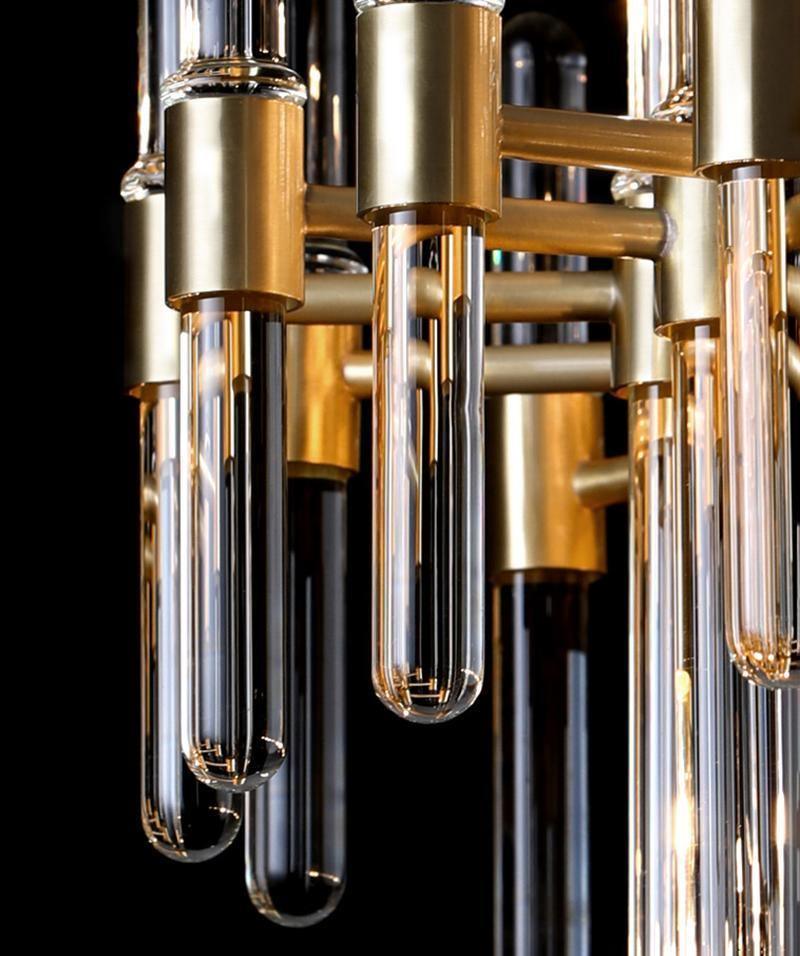 Brass sockets and clear glass tubes with rounded ends, seen close up on this Clérachic chandelier against a black backdrop.