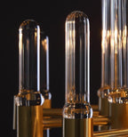 Tall rounded glass tubes rising from brass collars on this Clérachic chandelier, seen close up with warm light behind.