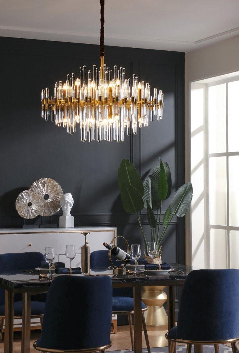 This Clérachic chandelier lit above a dark dining table with navy chairs, against a dark grey wall and a tall window.