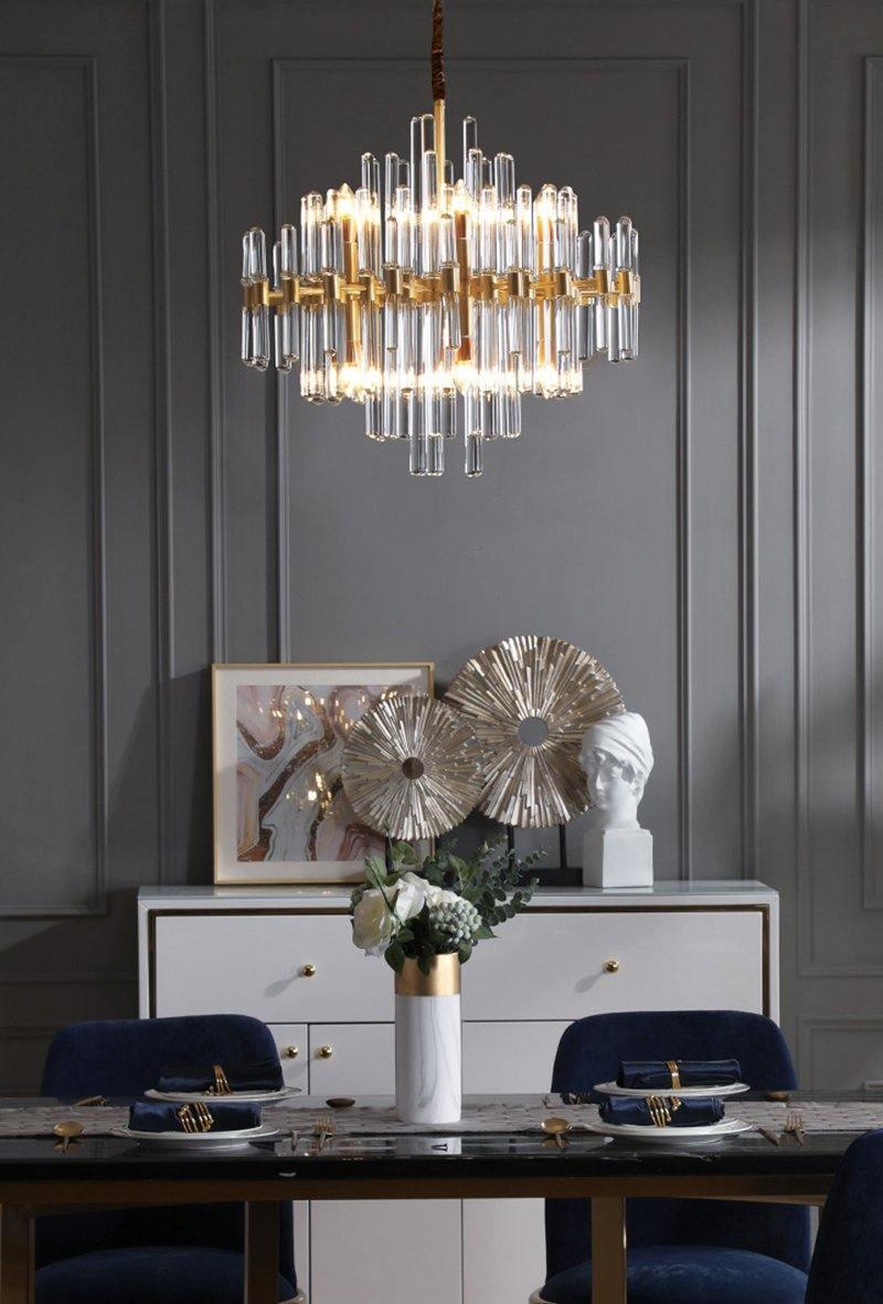A Clérachic chandelier hangs in a grey panelled room, above a white sideboard with silver wall decor, flowers and a navy chair set.