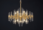 Clérachic brass chandelier lit on black, its bulbs and upper and lower glass rods spread wide in a flat, round shape.