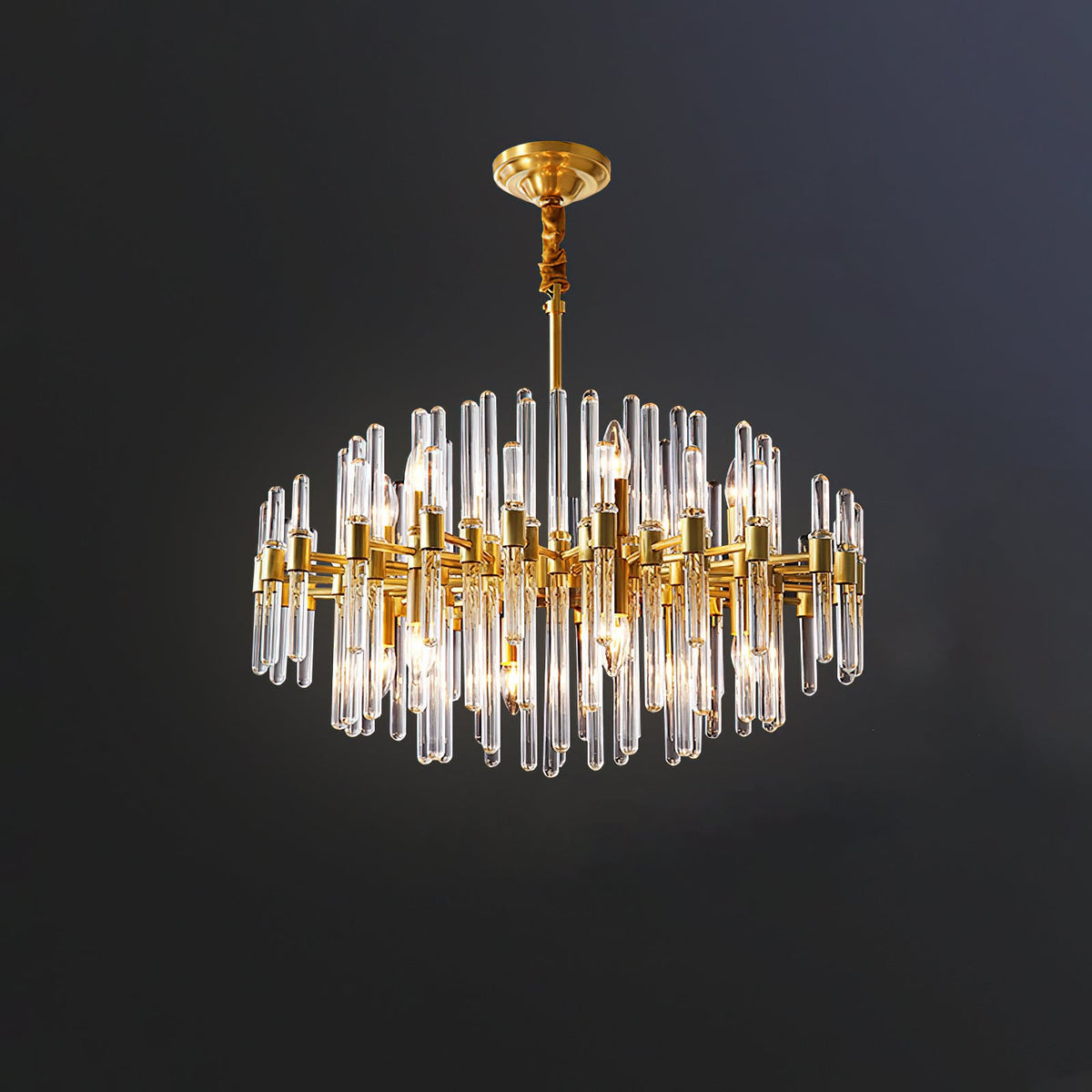 This Clérachic chandelier lit against a dark blue-grey wall, with its brass arms, covered chain and clear glass rods in a round form.