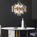 Against a dark wall, this Clérachic chandelier hangs above a round white marble table with a tall white vase and a gold base.