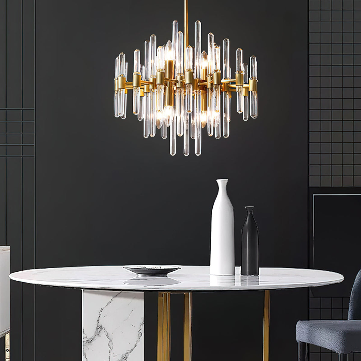 Against a dark wall, this Clérachic chandelier hangs above a round white marble table with a tall white vase and a gold base.