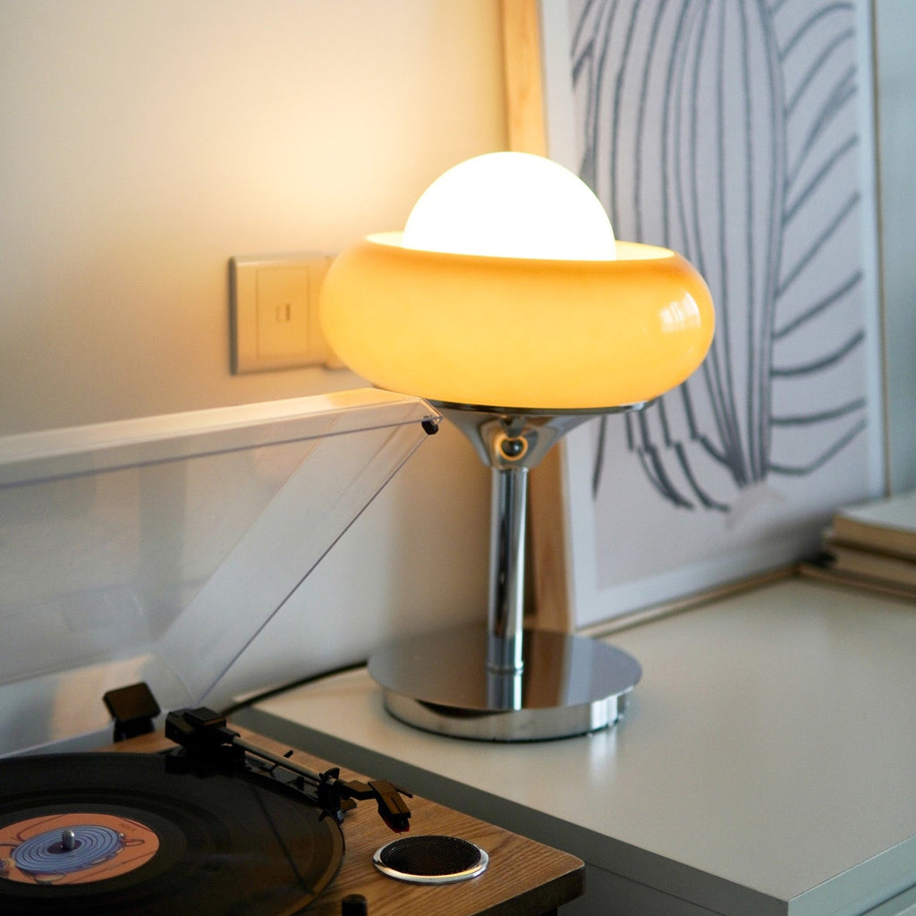 Lit on a white shelf beside a record player, this Clérachic table lamp glows warm from its amber glass shade and white globe.