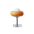 Plain white backdrop view of a Clérachic table lamp, its amber glass shade, white globe and flared chrome stem unlit.