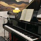 Small in the distance on top of a black piano, this Clérachic table lamp glows beside an open book of sheet music.