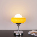 A bright yellow-amber Clérachic table lamp lit on a dark surface, its white globe glowing above the chrome base.