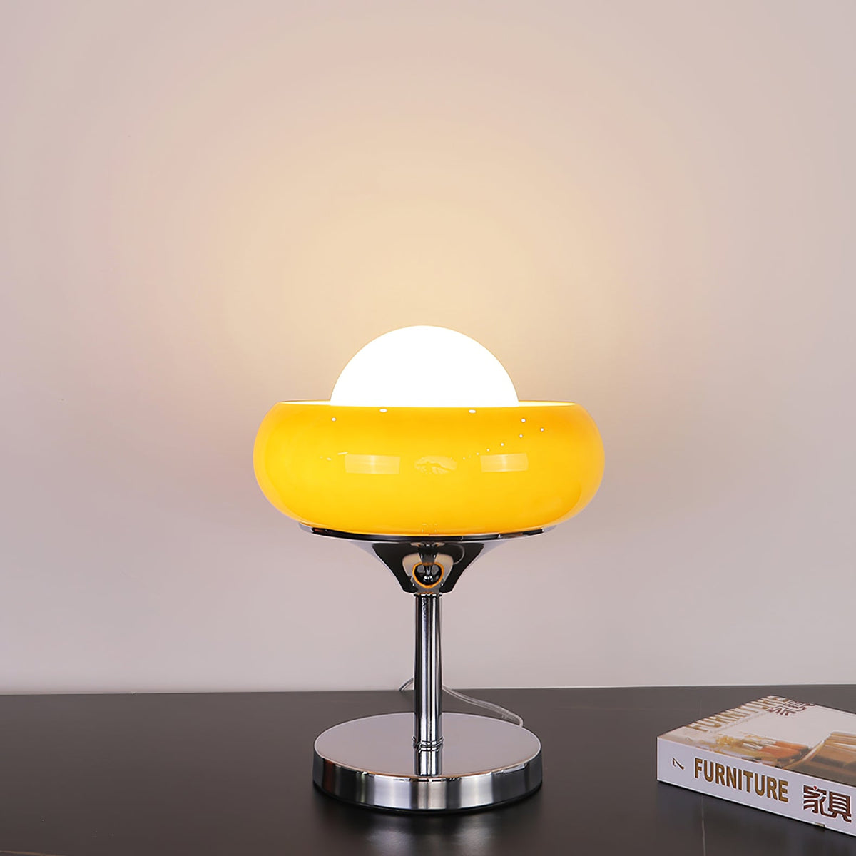 A bright yellow-amber Clérachic table lamp lit on a dark surface, its white globe glowing above the chrome base.